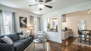 A living room with a sofa, coffee table, and a dining area with chairs and stools. - Cottage on Broadmoor (Gulfport)