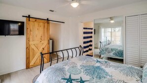 Un dormitorio con cama, puerta de madera, ventilador de techo y espejo.