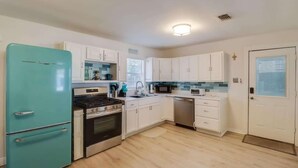 Una cocina con armarios blancos, un refrigerador turquesa, estufa, microondas y lavavajillas.