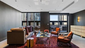 Ein modernes Wohnzimmer mit einer Couch, Sesseln, einem Couchtisch und Blick auf hohe Gebäude.