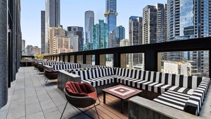 Eine Dachterrasse mit einer schwarz-weiß gestreiften Sitzgelegenheit, einem kleinen Tisch und einem Stuhl.