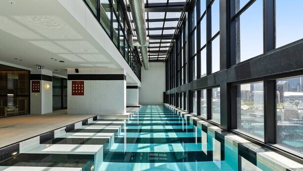 Ein moderner, überdachter Swimmingpool mit Glaswänden und Blick auf die Stadtlandschaft.