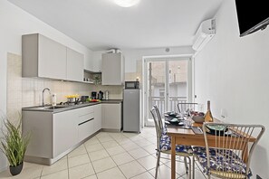 A modern kitchen with white cabinets, a built-in microwave, and a dining area with a wooden table and metal chairs. - Casa Vergolano, Arco, Italy (Arco)