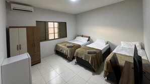 A room with two beds, a wardrobe, a television, and an air conditioning unit. - Alvorada Hospedagem (Jataí)