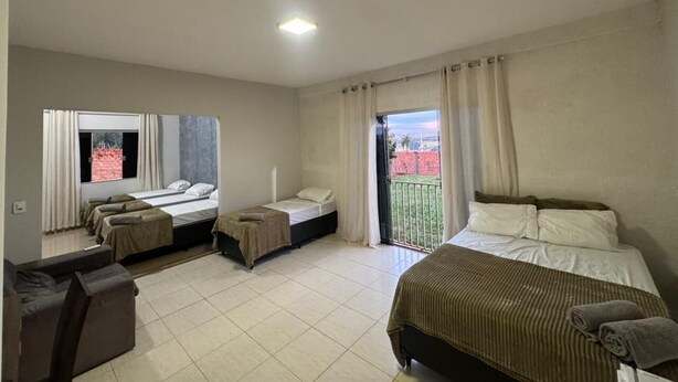 A hotel room with a bed, a sofa, a small table, and a balcony with a view. - Alvorada Hospedagem (Jataí)