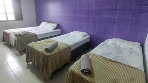 A room with four single beds, each with a rolled towel, a window, and a purple wall. - Alvorada Hospedagem (Jataí)