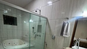 A modern bathroom with a glass-enclosed shower, a standalone bathtub, a toilet, and a vanity with two sinks. - Alvorada Hospedagem (Jataí)