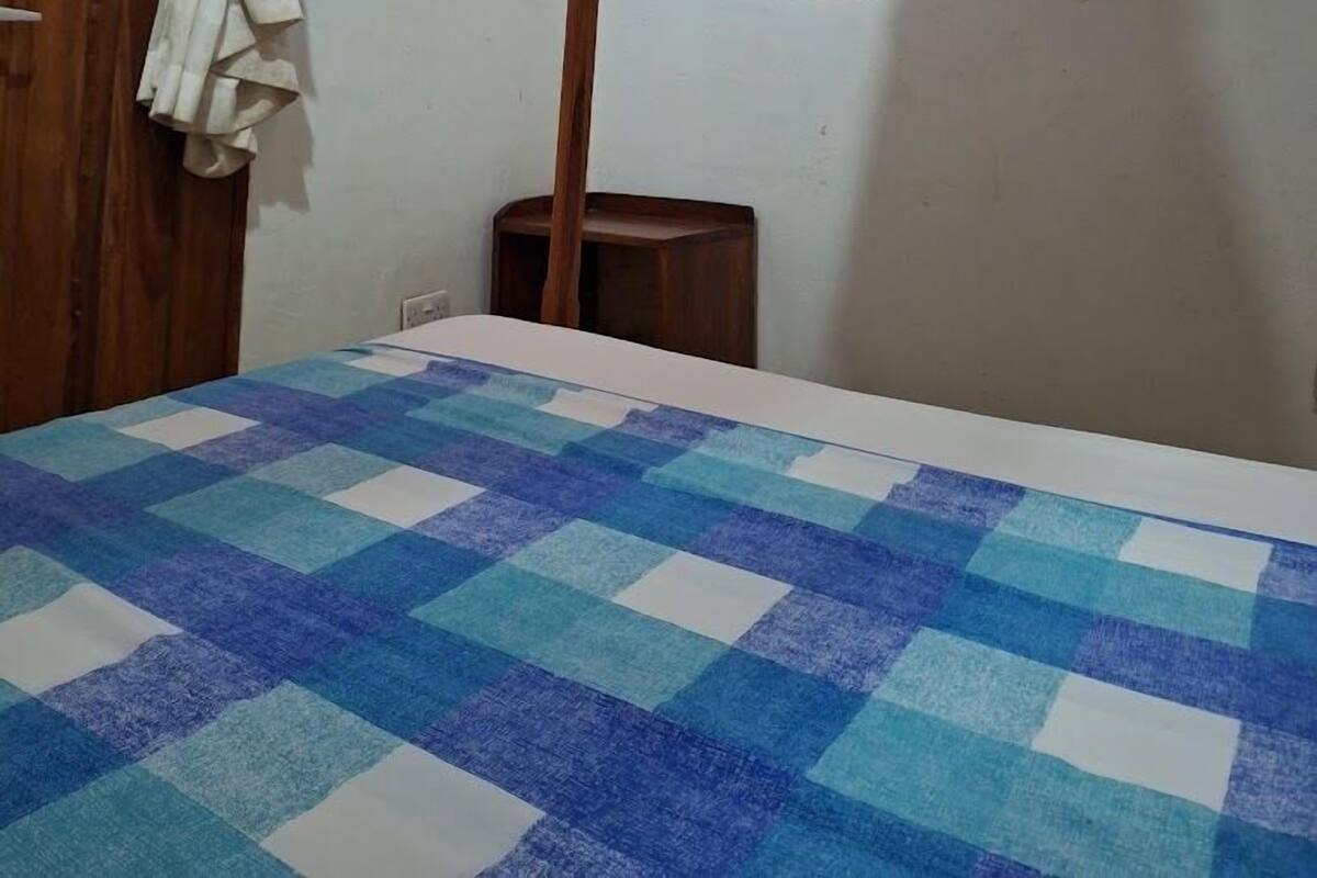 Un dormitorio con edredón a cuadros, cabecero de madera y cortina atada en la parte superior.