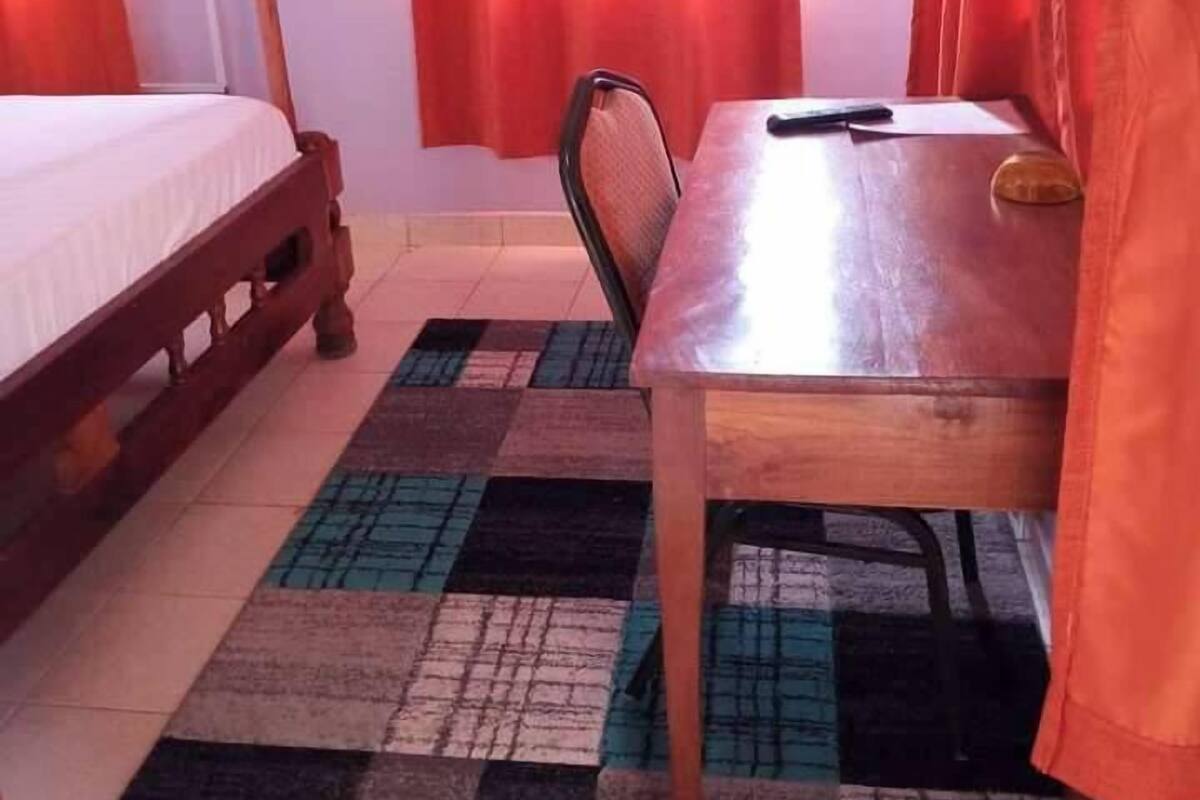 Una habitación con una cama, una mesa, una silla, un televisor y una ventana con cortinas.