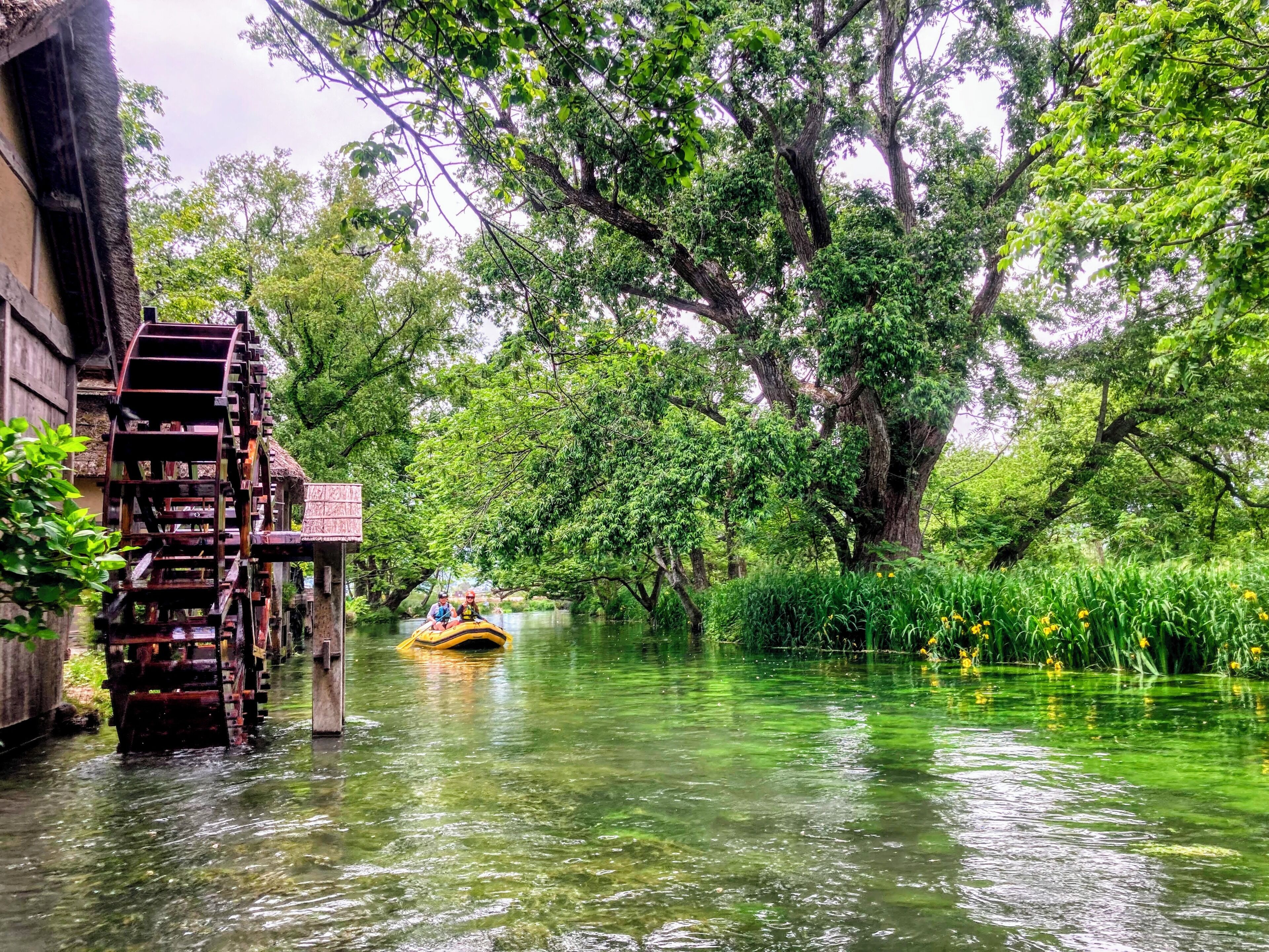 A river with a wooden water wheel and a yellow boat.