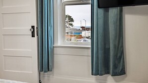 Et værelse med en hvid dør, et vindue med blå gardiner og udsigt til en gade med bygninger og en bil.
