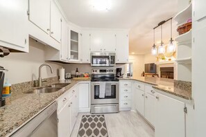Eine moderne Küche mit weißen Schränken, Edelstahlgeräten, Granit Arbeitsplatten und einem gemusterten Teppich.