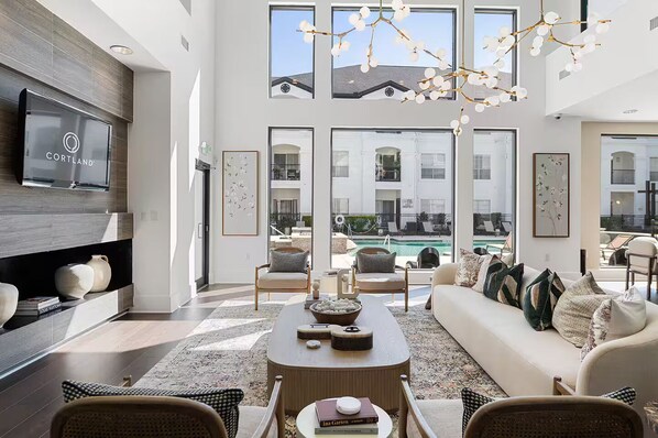 A spacious living room with a large TV, comfortable seating, a pool view, and a modern chandelier. - Chic 2BR Apartment Minutes to Montrose (Houston)