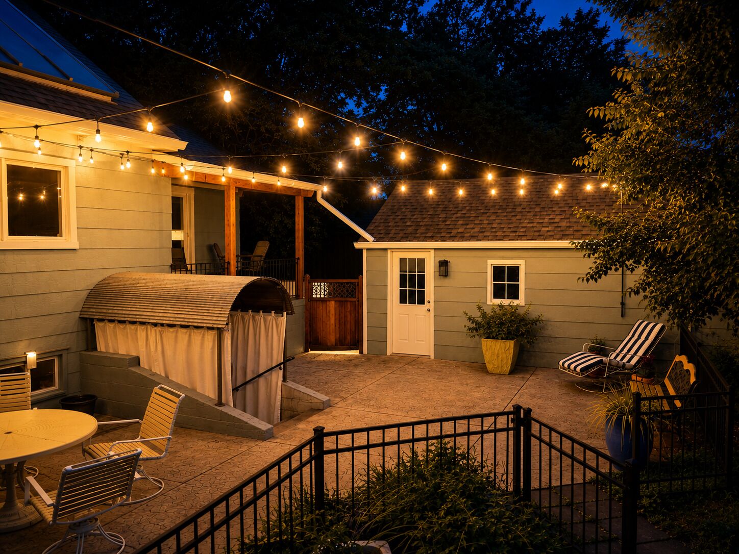 Eine überdachte Terrasse im Freien mit Lichterketten, einem Grill und Gartenmöbeln.