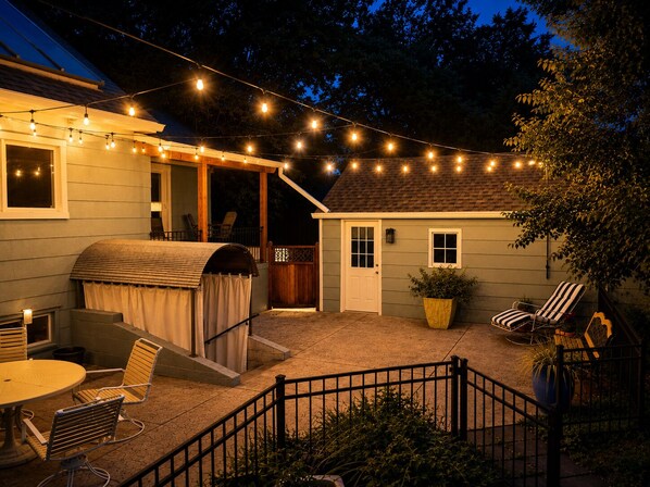 A covered outdoor patio with string lights, a barbecue grill, and outdoor seating.