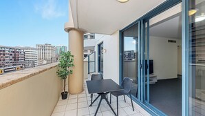 Un balcón con mesa y sillas, una planta en maceta y vistas a la ciudad.