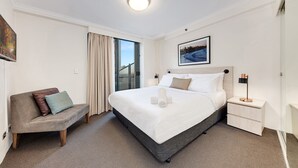 Una habitación de hotel con cama, sofá, mesita de noche, lámpara y un cuadro en la pared.