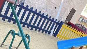 Een speeltuin met een wipkippen, een glijbaan en een zandbak.