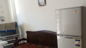 Een kleine kamer met een bed, een koelkast, een klok en een bureau met een computer.