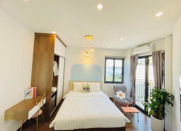 Habitación de hotel con cama, escritorio, silla, planta en maceta y vistas al exterior.