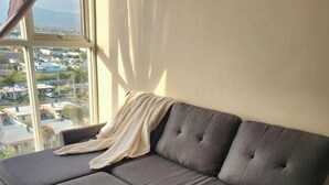 Ein graues Sofa mit Fußhocker, ein Fenster mit Blick auf Gebäude und ein Vorhang.