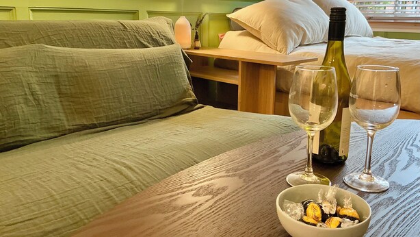 Ett rum med en grön soffa, ett träbord med en vinflaska, två vinglas och en skål med chokladpraliner.