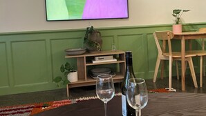 Ett rum med en tv som är monterad på väggen, ett träbord med stolar, en krukväxt och två vinglas på ett bord.