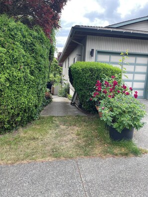 Ein Auffahrt, die zu einem Haus mit Garage führt, umgeben von gepflegten Hecken und blühenden Pflanzen.