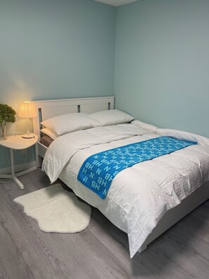 A bedroom with a bed, a nightstand, a lamp, and a white rug. - Anna's cozy house (Delta)