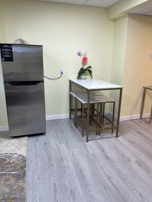 A compact kitchenette with a stainless steel refrigerator, a marble-top table, and a small potted plant. - Anna's cozy house (Delta)