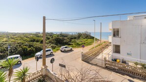 A coastal road with parked cars, a white building with a balcony, and a view of the sea. - Buena Vista - Sea Oasis Residence (Salve)