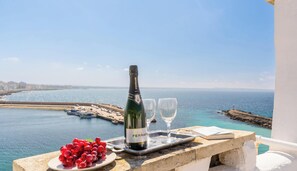 Une bouteille de vin Ferrari Brut, deux verres et une assiette de raisins rouges sur un balcon donnant sur une vue côtière.