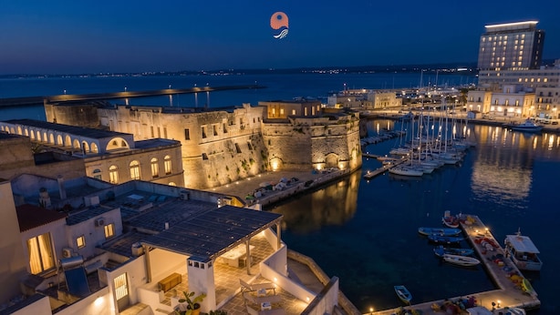 Un pueblo costero con un fuerte histórico, un puerto deportivo con barcos y edificios con terrazas.