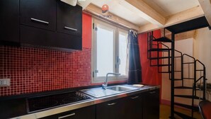Une cuisine avec un mur recouvert de carreaux rouges, des meubles noirs, un évier en acier inoxydable et un escalier noir.