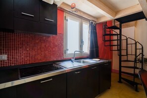 Una cucina con zoccolo in piastrelle rosse, pensili neri, lavello in acciaio inossidabile e una scala nera.