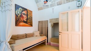 Une pièce avec un lit, un tableau, une porte et un mur en pierre.