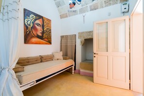 Una stanza con un letto, un quadro, una porta e un muro in pietra.