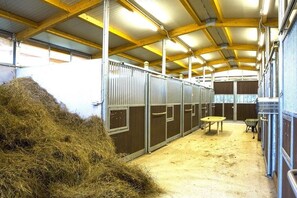 Een stal met metalen boxen, hooirollen en een tafel.