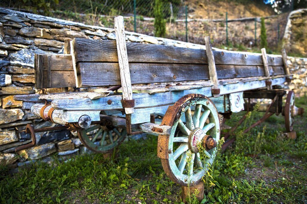 A rustic wooden cart with metal wheels, leaning against a stone wall.
