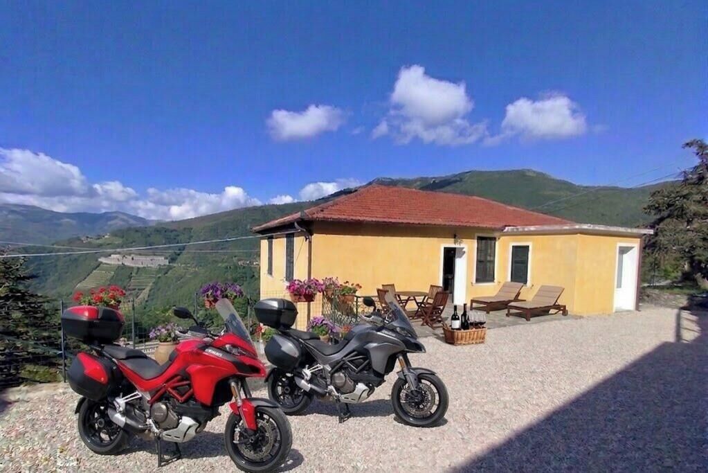 Two motorcycles parked in front of a yellow building with a red roof, overlooking a mountainous landscape.