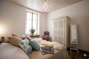 Ein Schlafzimmer mit Bett, Fenster, Heizkörper, Spiegel und einer Pflanze.