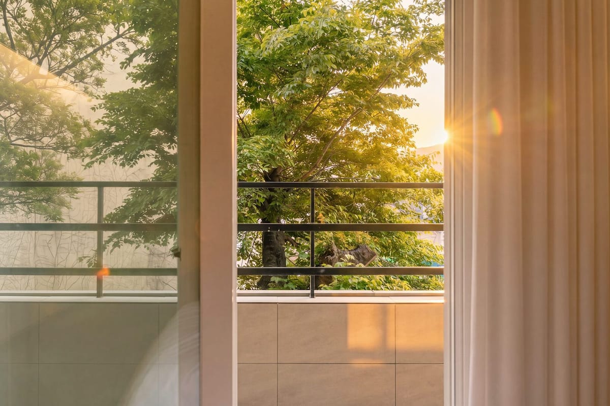 Ein Zimmer mit großem Fenster, Blick auf Bäume und Fliesenboden.