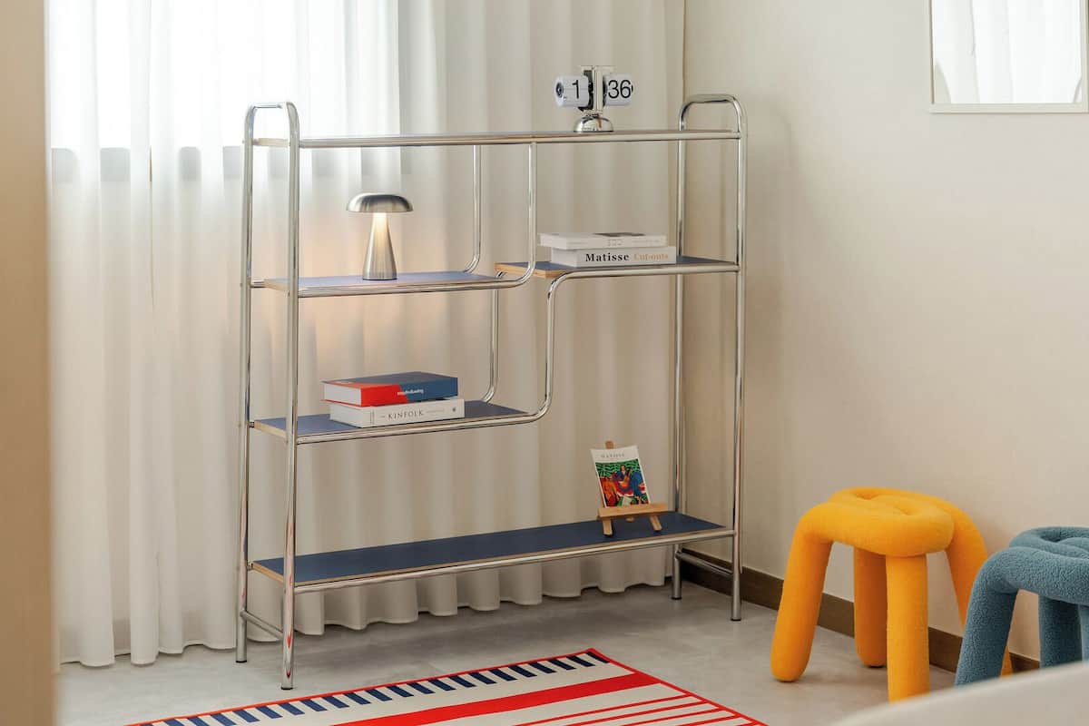 Ein Zimmer mit einem Metallregal, einem kleinen Hocker, einem blauen Handtuch und einem Streifen Teppich.