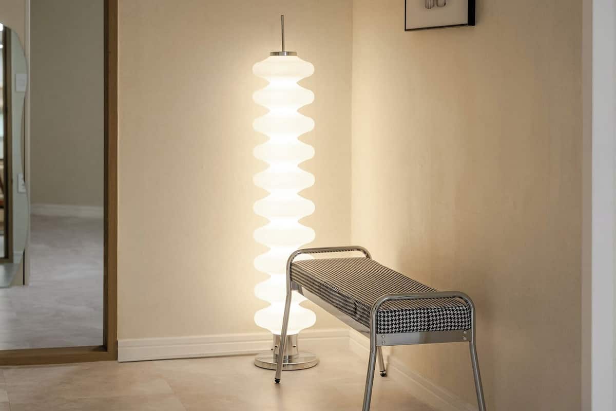 Ein modernes Interieur mit einer hohen, spiralförmigen Stehlampe, einer Metallbank und einem gerahmten Bild an der Wand.