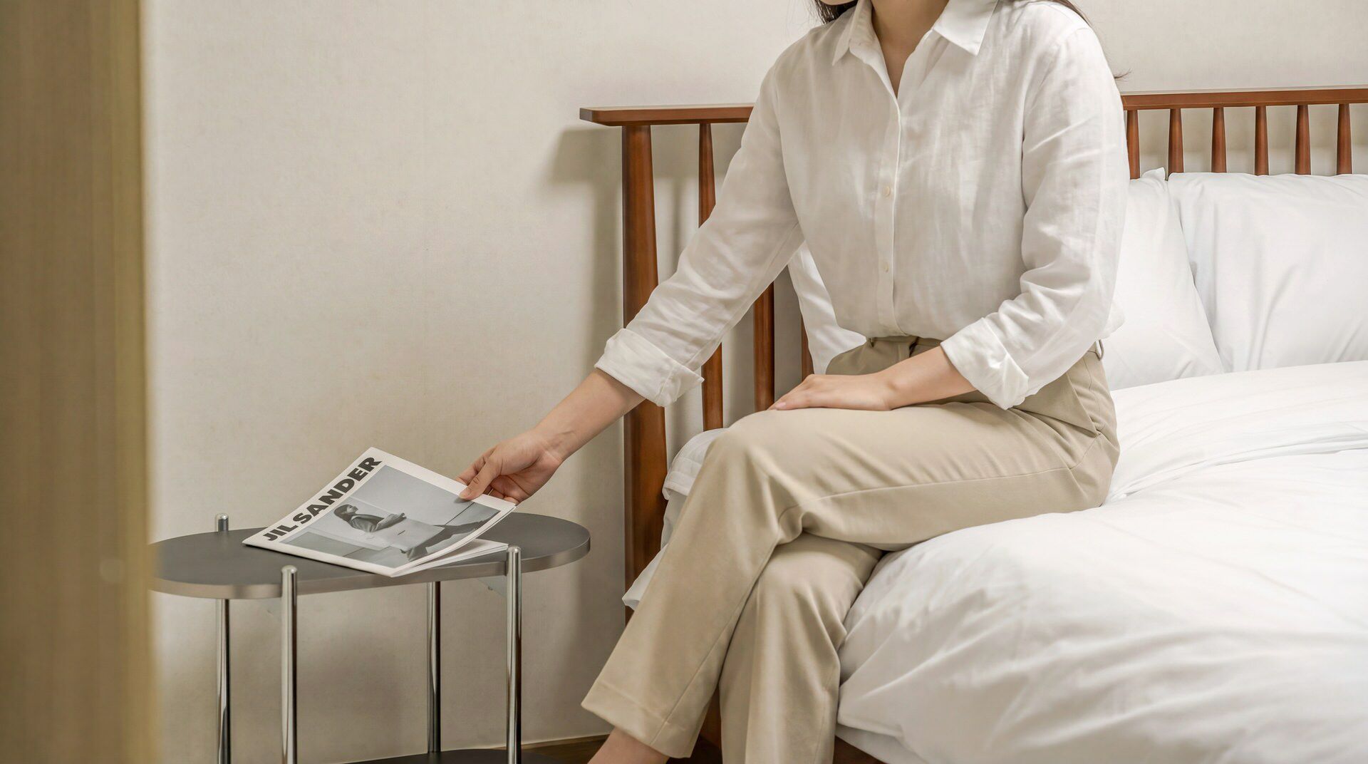 A person sitting on a bed in a room with a wooden headboard, reading a magazine.