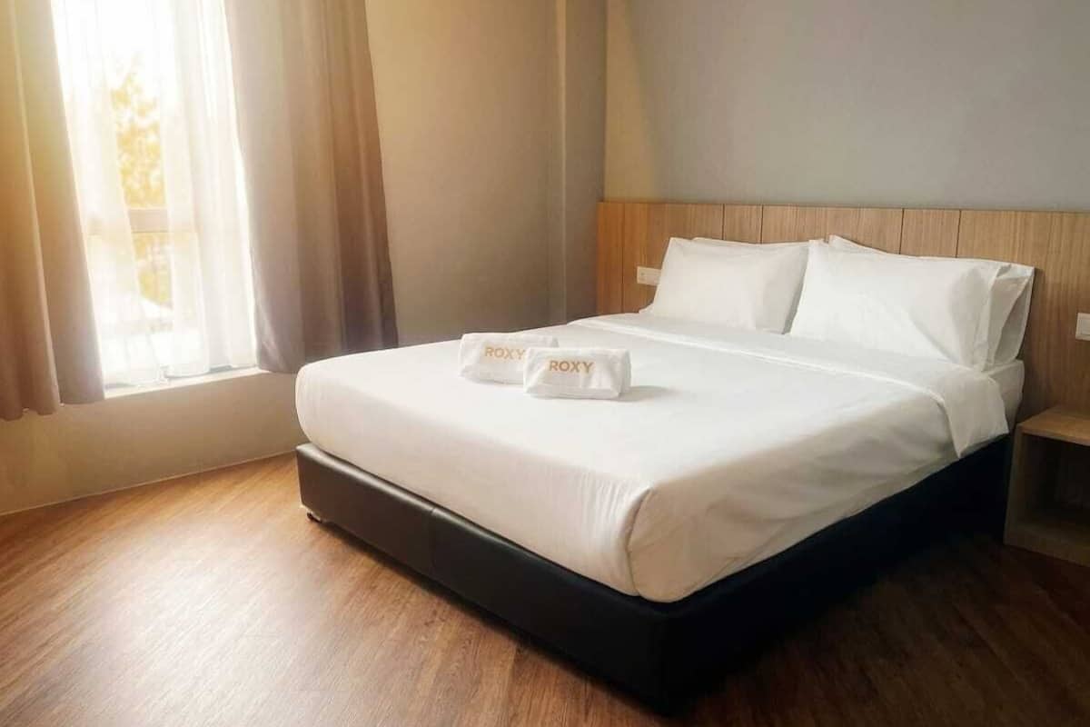 Una cama bien hecha con sábanas blancas y un cabecero de madera, una mesita de noche y una ventana con cortinas.