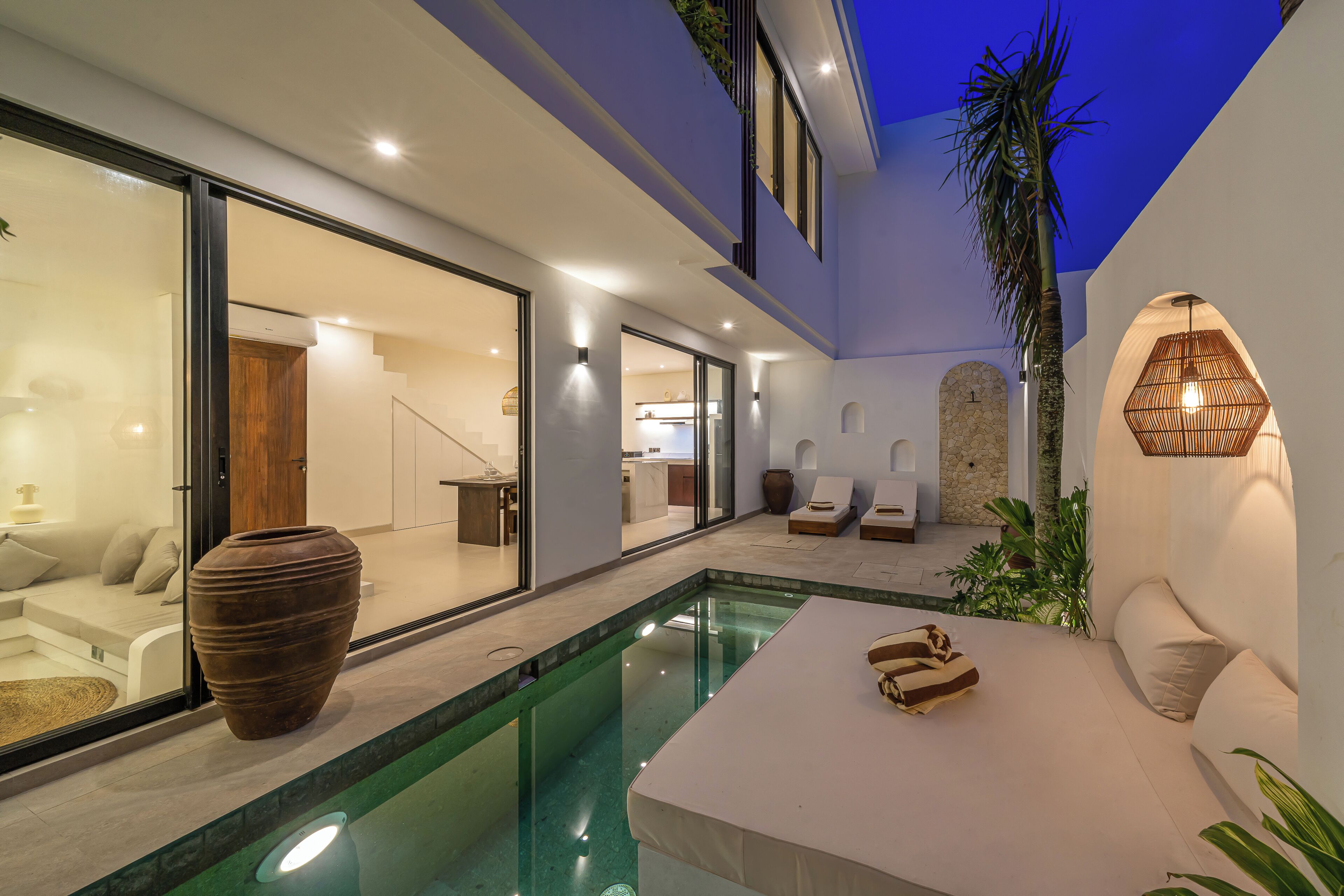 Un espace piscine extérieur moderne, doté d’un coin salon, d’un grand vase et d’un luminaire suspendu.