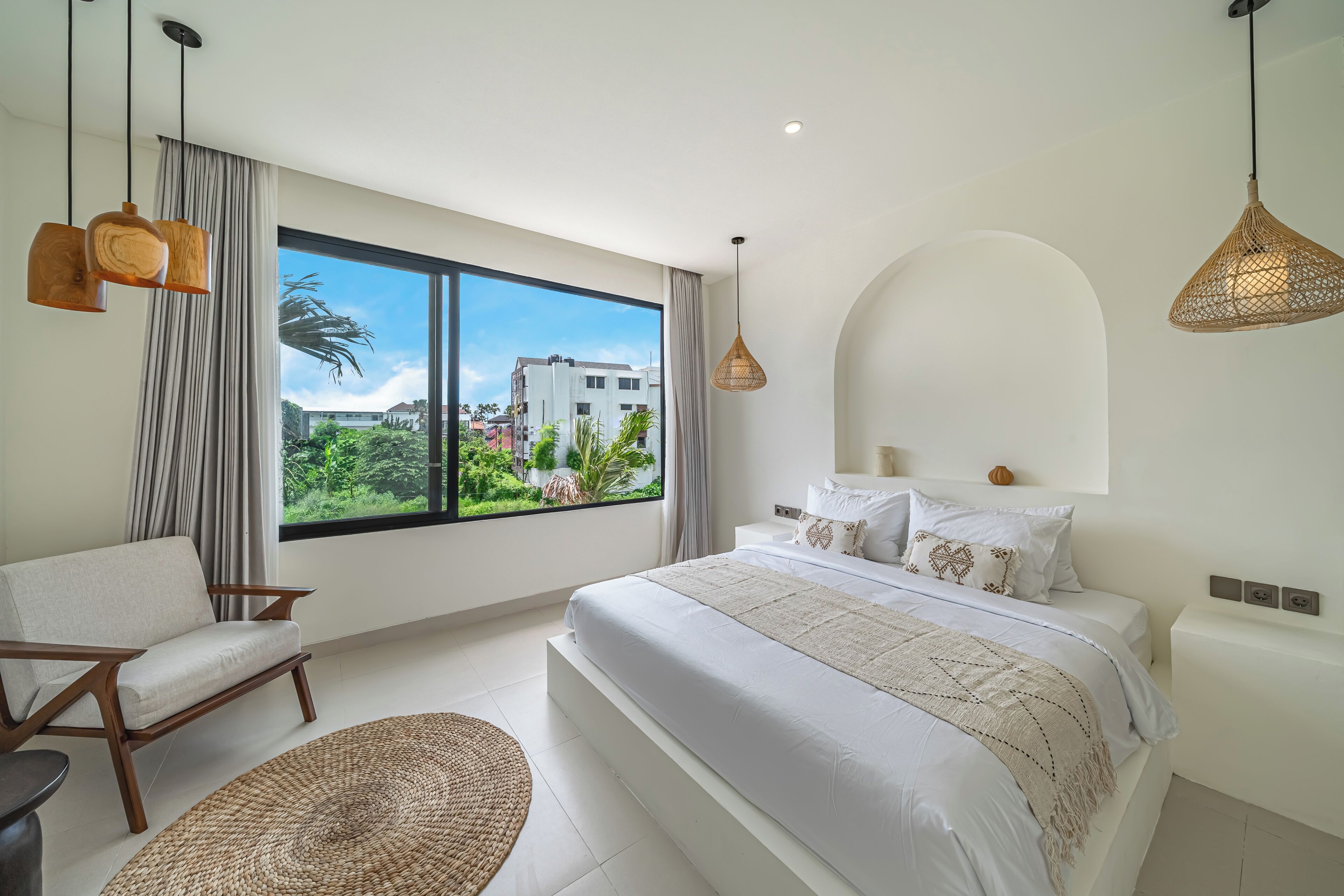 Une chambre moderne avec une grande fenêtre, un lit, une chaise et un luminaire suspendu.