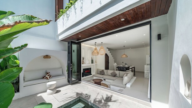 Una casa moderna con piscina, un salón con sofá y televisor, y una escalera que lleva a un balcón.