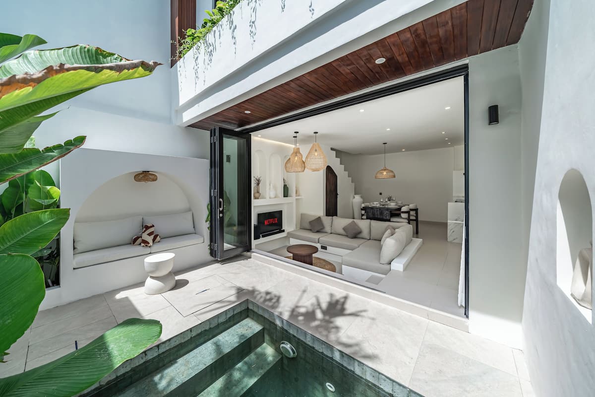 Une maison moderne avec une piscine, un salon doté d’un canapé et d’une télévision, et un escalier menant à un balcon.